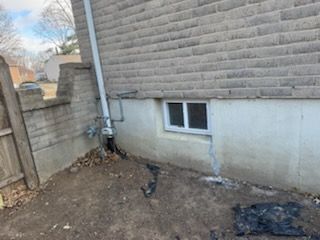 Exterior of a brick building with a window and a vertical pipe next to a brown, muddy ground.
