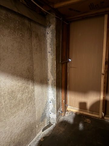 Concrete basement wall with vertical wooden frame. Water stains visible.