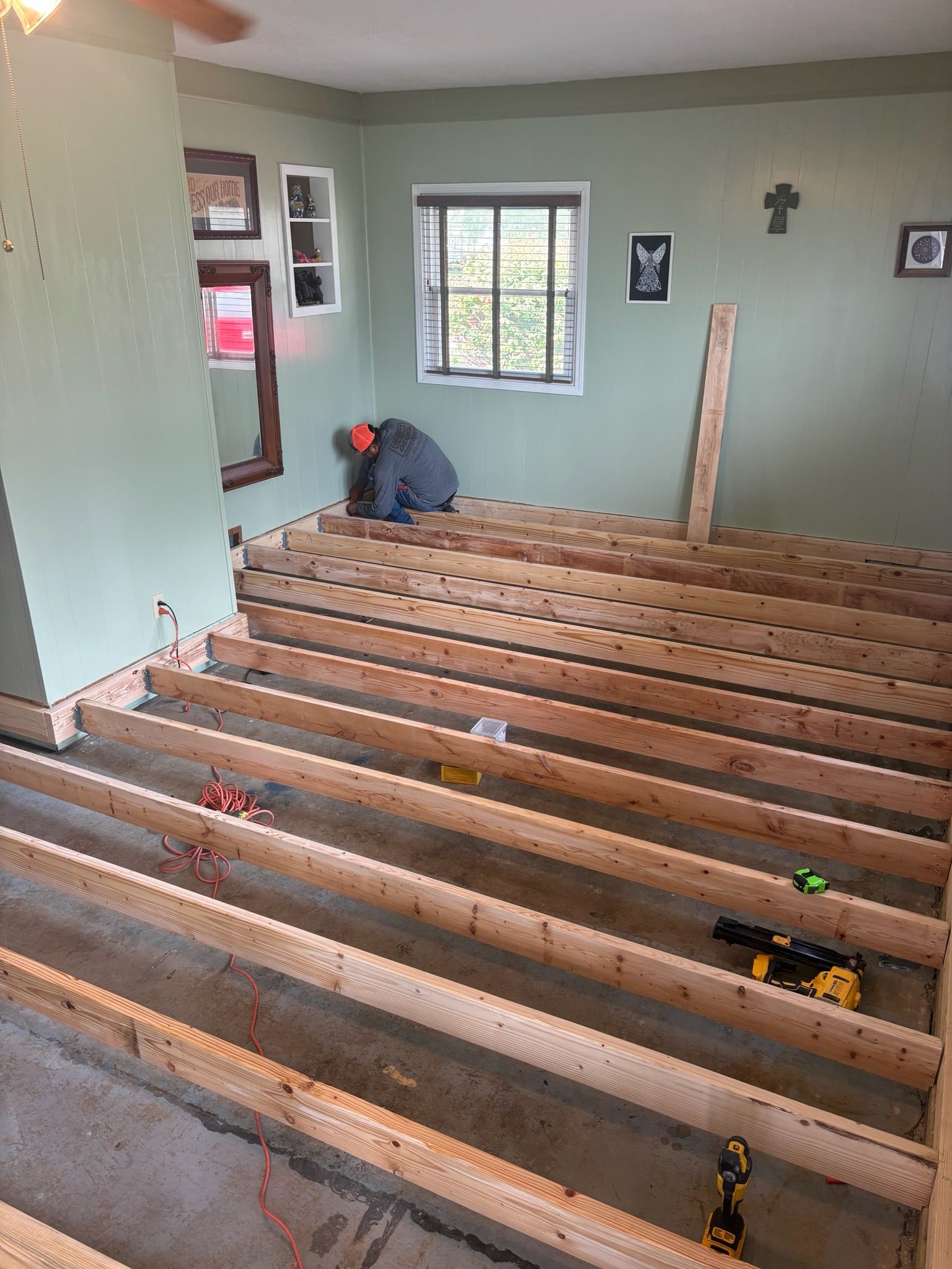A person installing wooden floor joists in a room with green walls and a window.