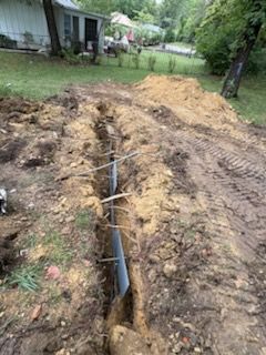 A trench dug in a yard with a silver pipe and wooden supports, likely for construction.
