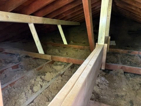 Attic interior with exposed wooden rafters, joists, and insulation.