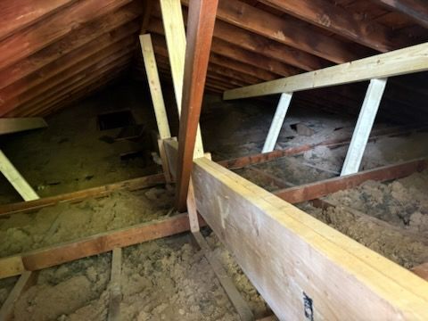 Attic interior with wooden beams and insulation. Sunlight filters through the rafters.