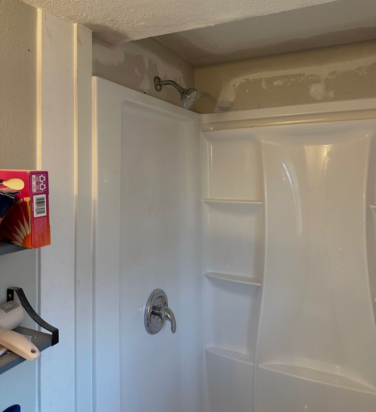 White shower stall with showerhead and faucet. Shower curtain pulled back.