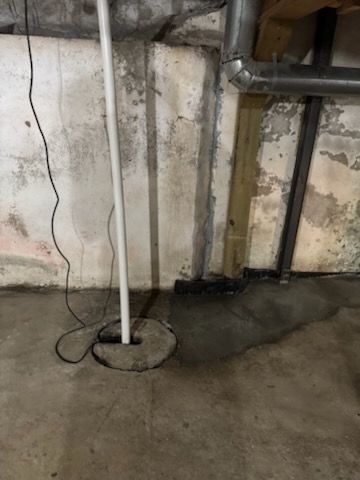 Concrete basement floor with a pole, pipes, and water stains on walls.
