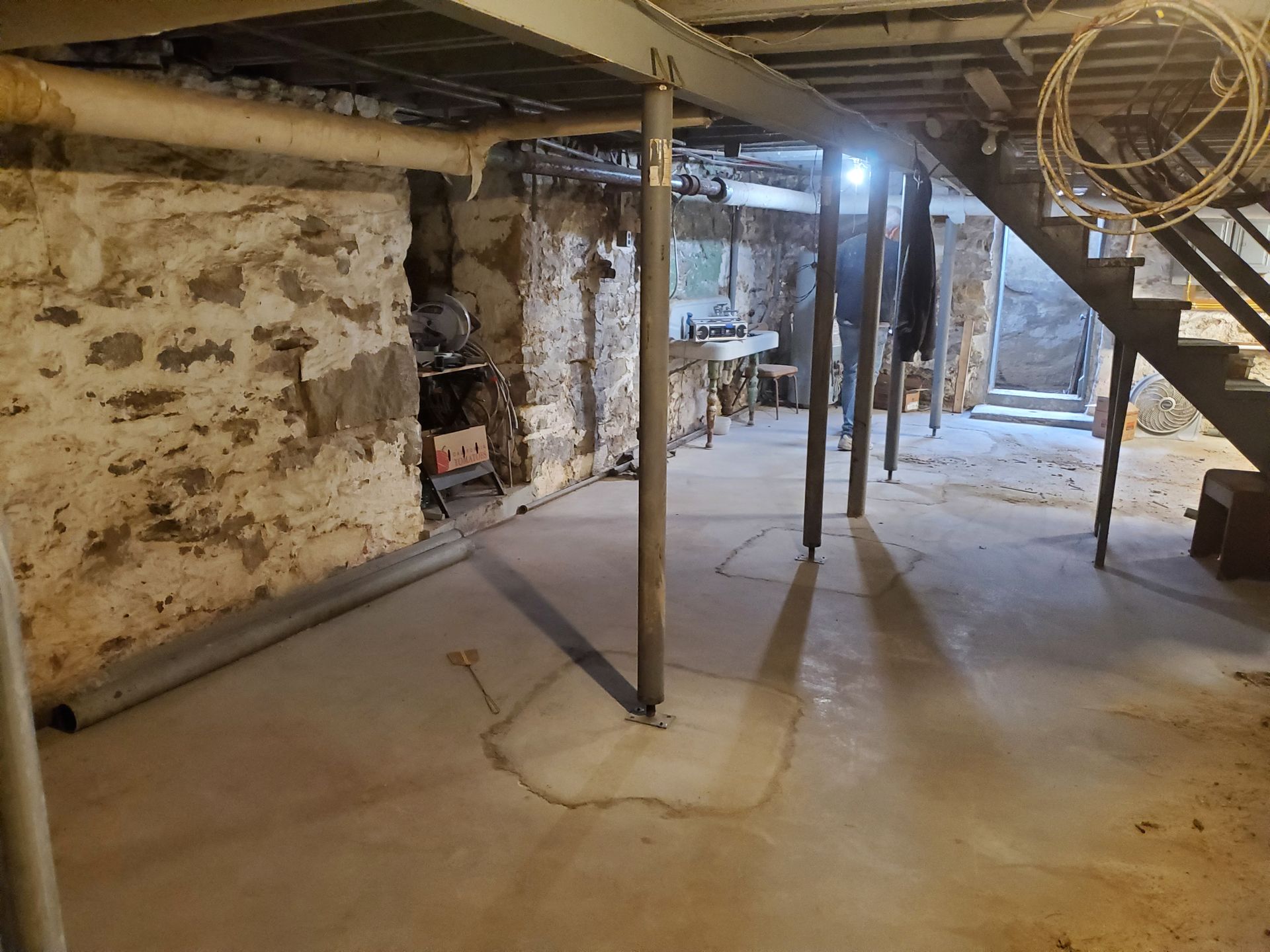 Basement with concrete floor, stone walls, steel support beams, and stairs.