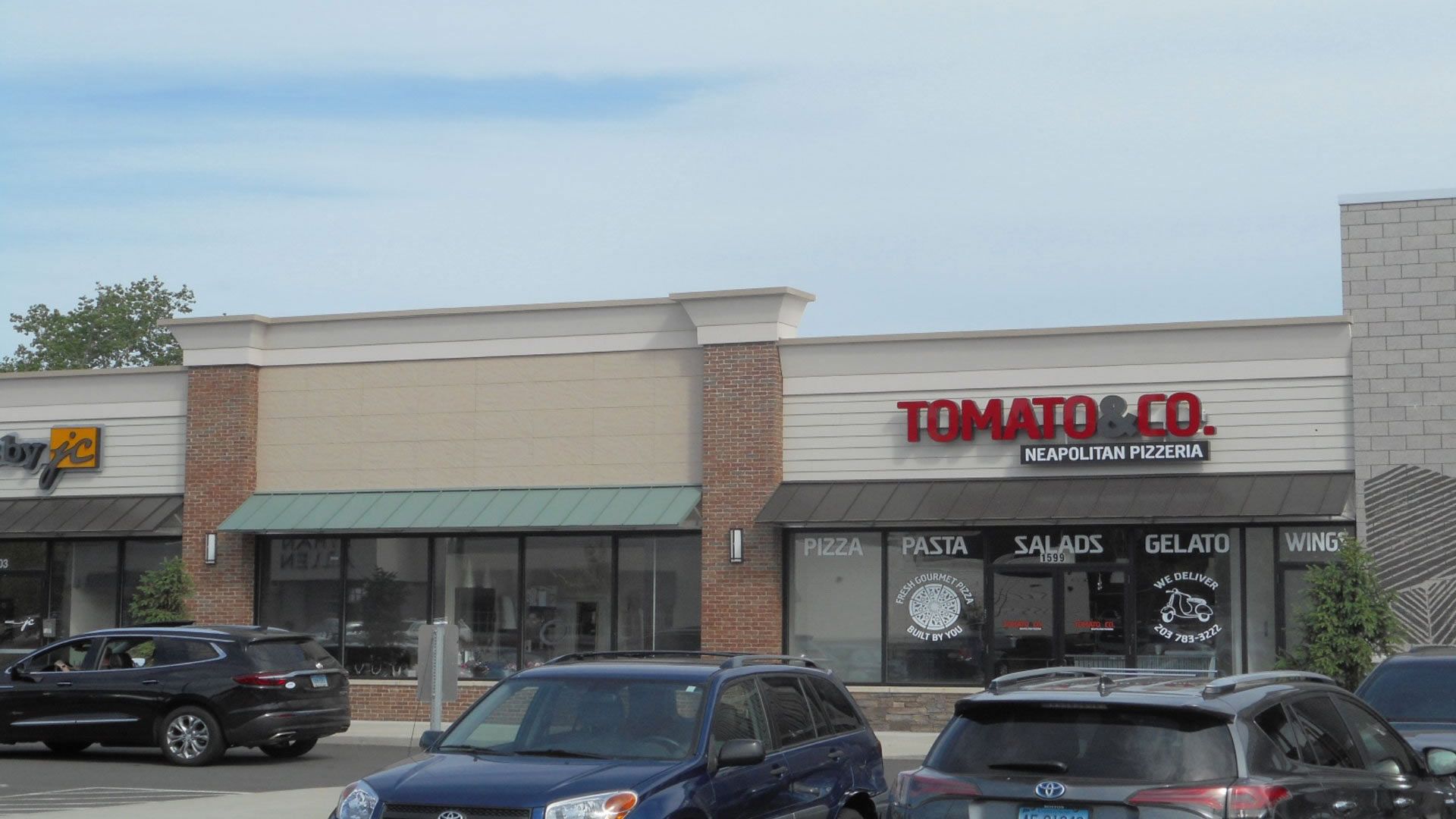 Exterior view of Tomato & Co. restaurant in a strip mall, with cars parked in front.