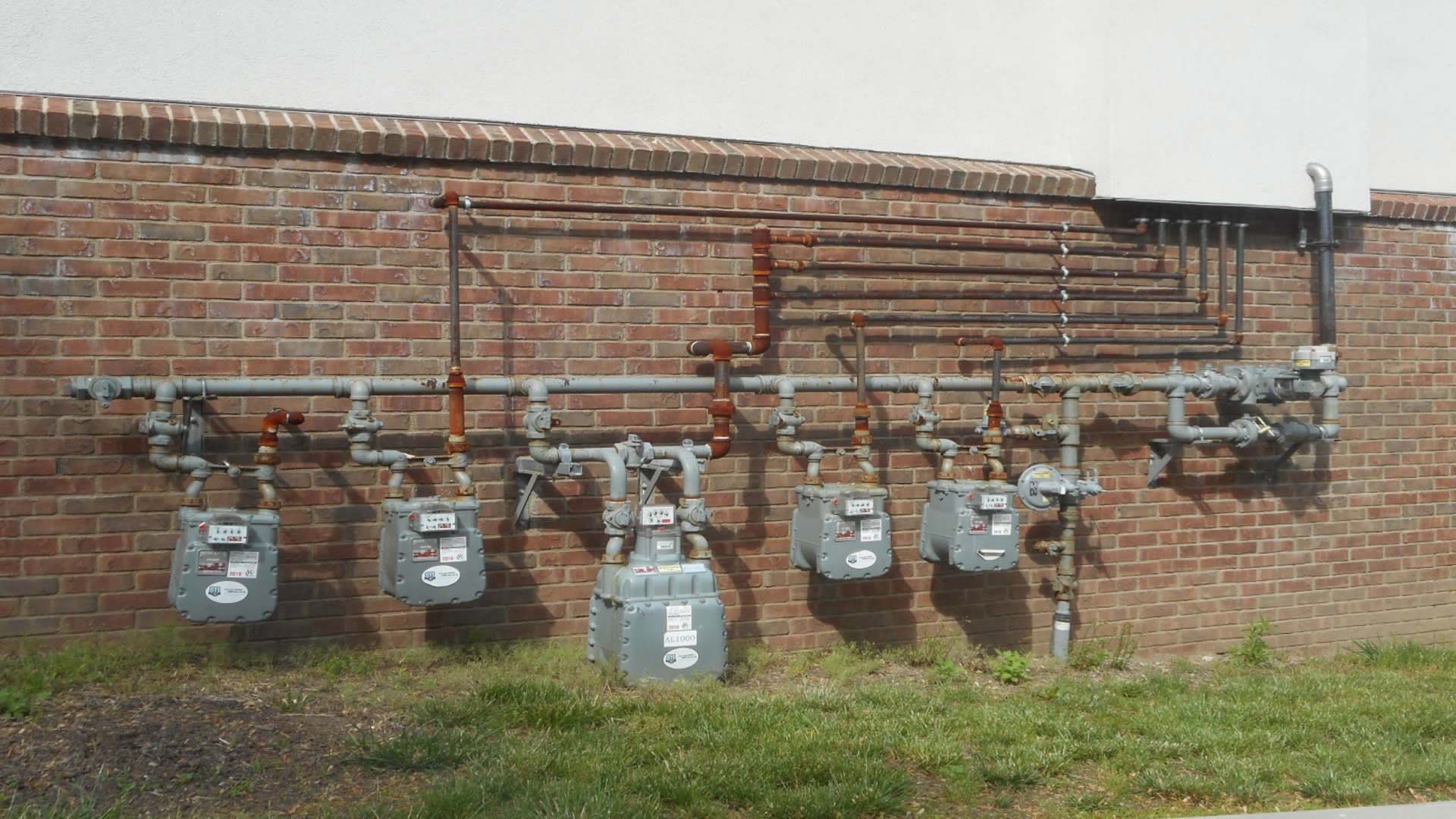 Five natural gas meters mounted on a brick wall with connected copper pipes.