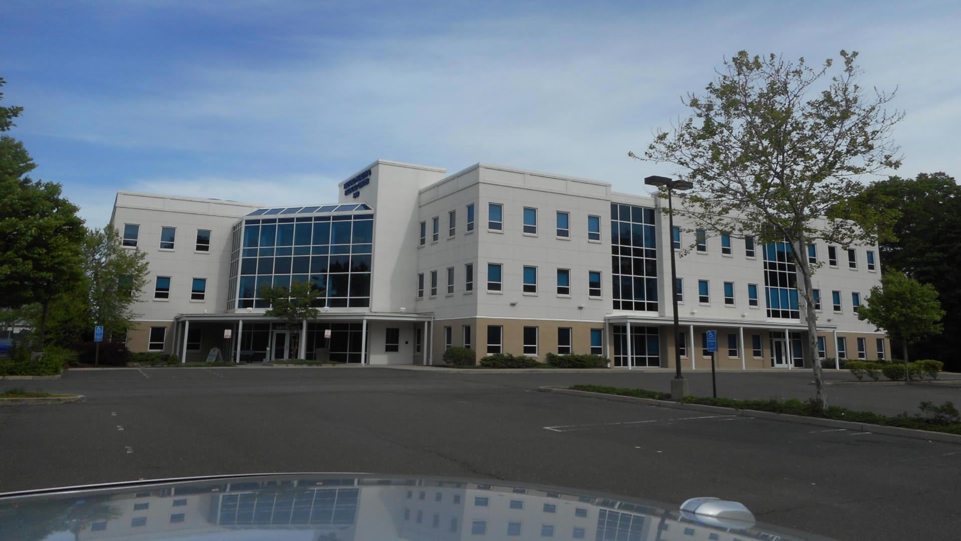 Modern white building with blue-tinted windows, set on a blacktop with clear blue sky.