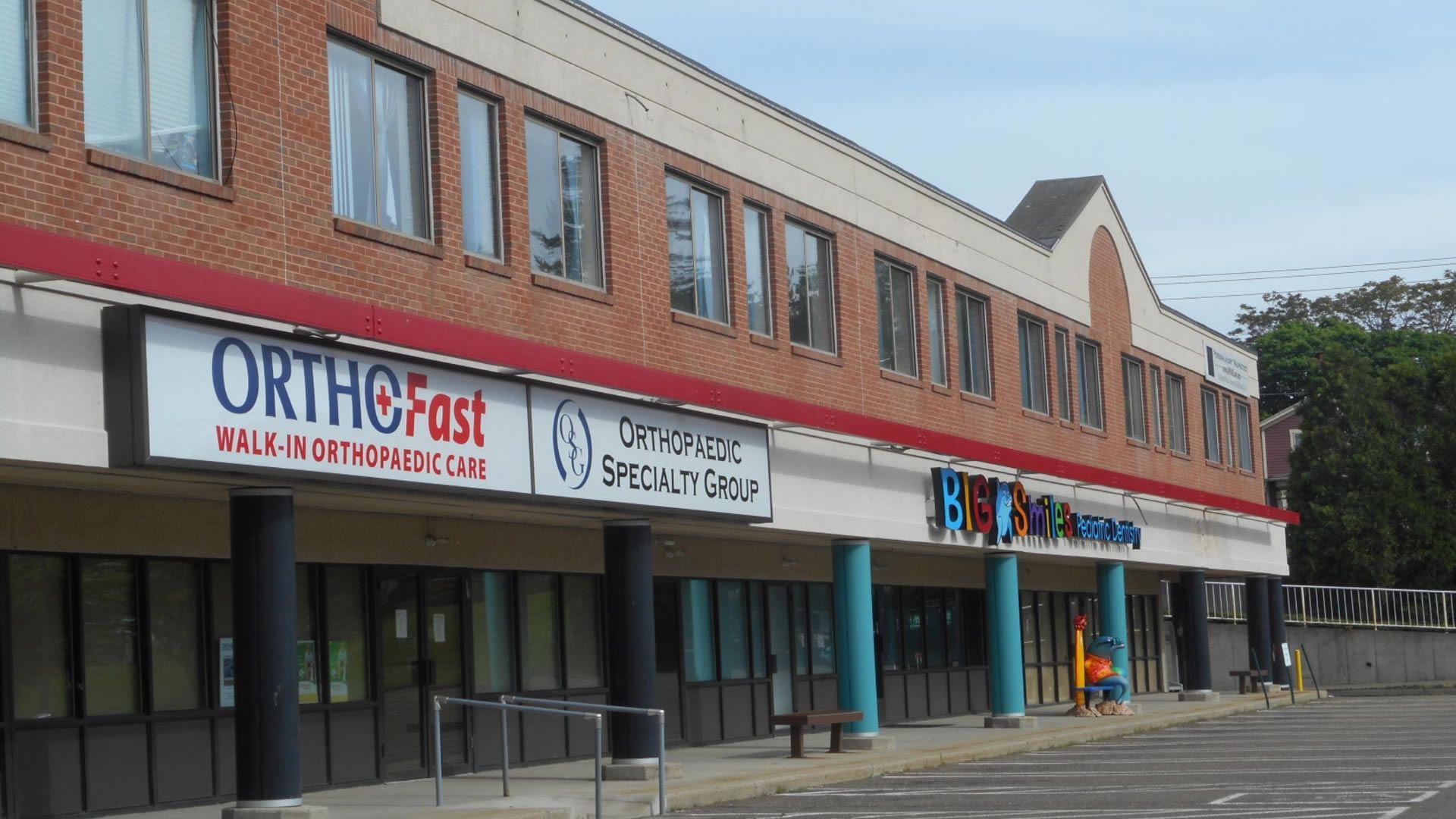 A strip mall with OrthoFast and other businesses; brick facade, blue and white signage.