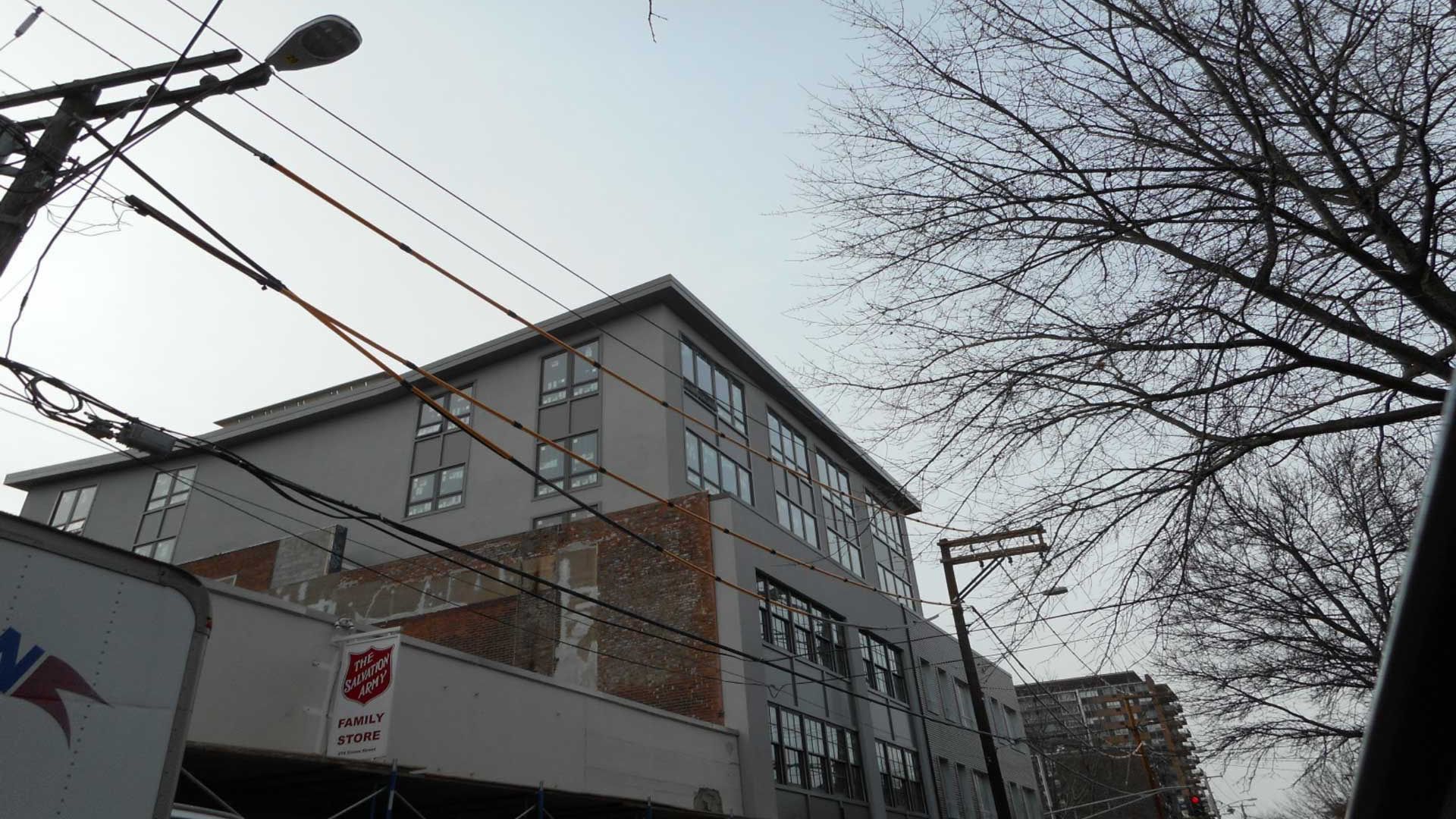 Gray apartment building under cloudy sky, with power lines and bare trees in view.