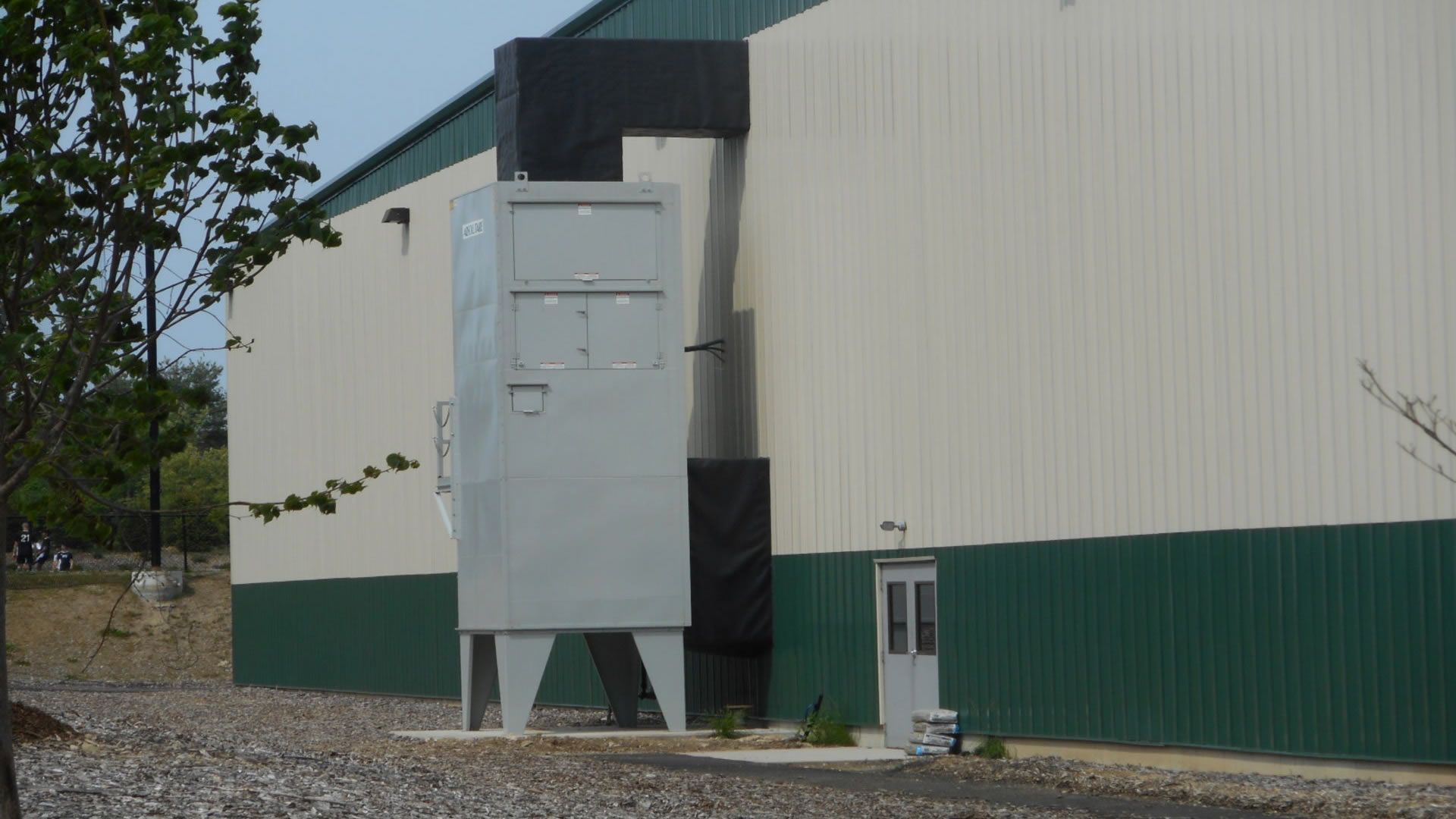 Gray industrial air filter unit on the exterior of a building with green and white siding.