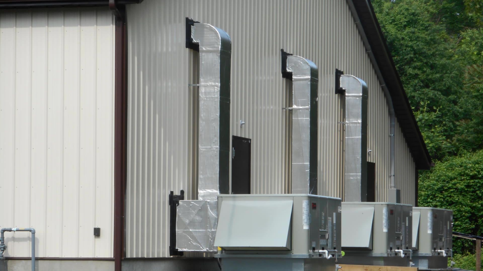 Exterior view of a building with four HVAC units, each having a silver exhaust duct attached to the wall.