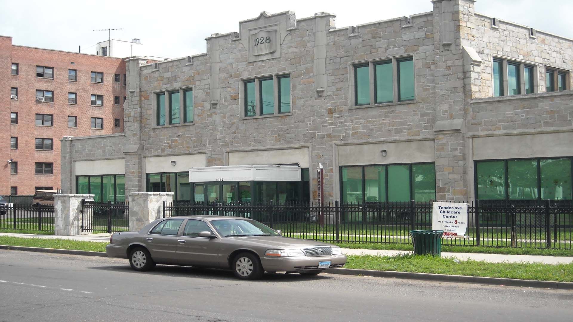 Gray brick building with large windows and a car parked in front.