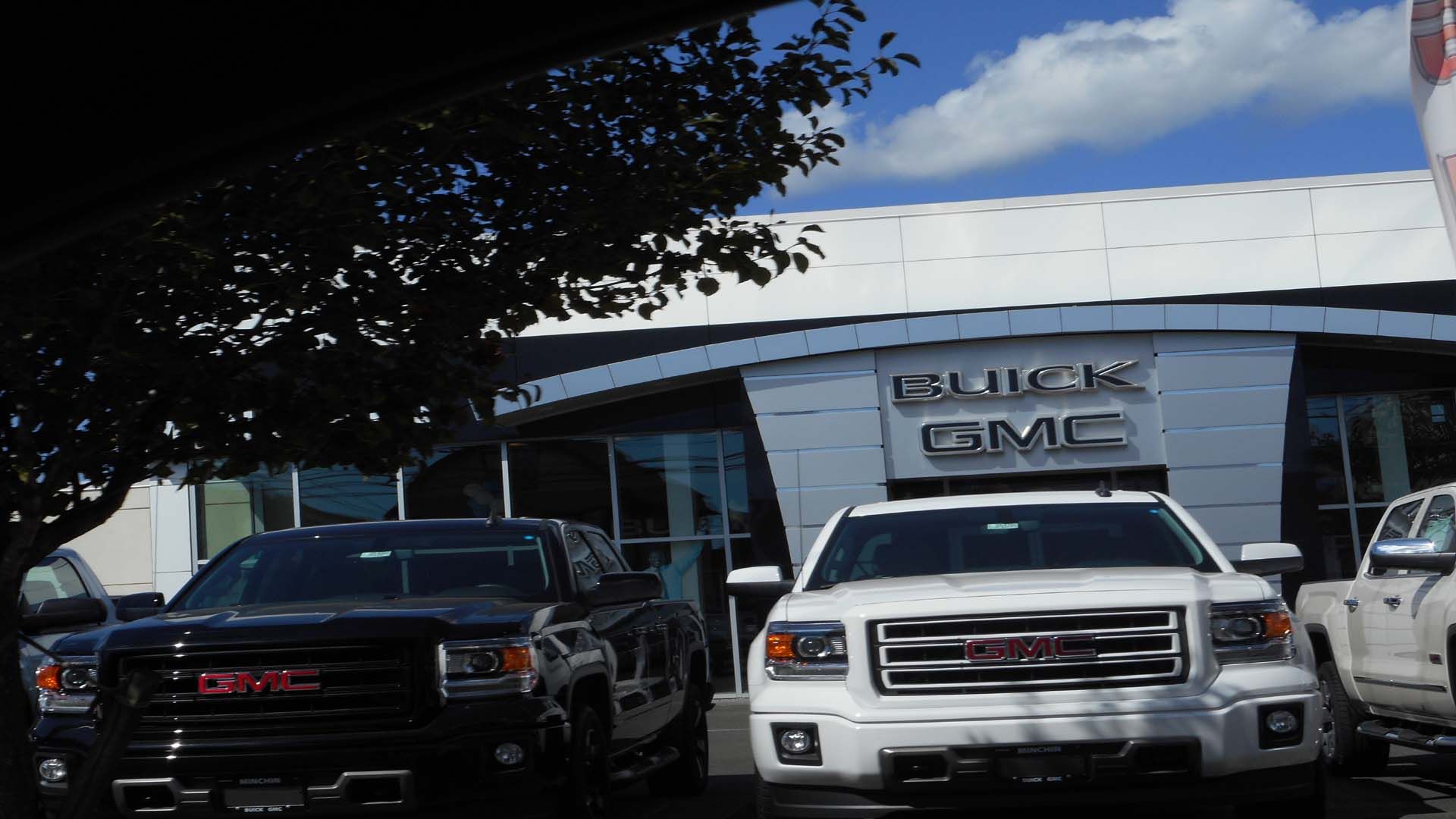 GMC trucks parked in front of a Buick GMC dealership on a sunny day.