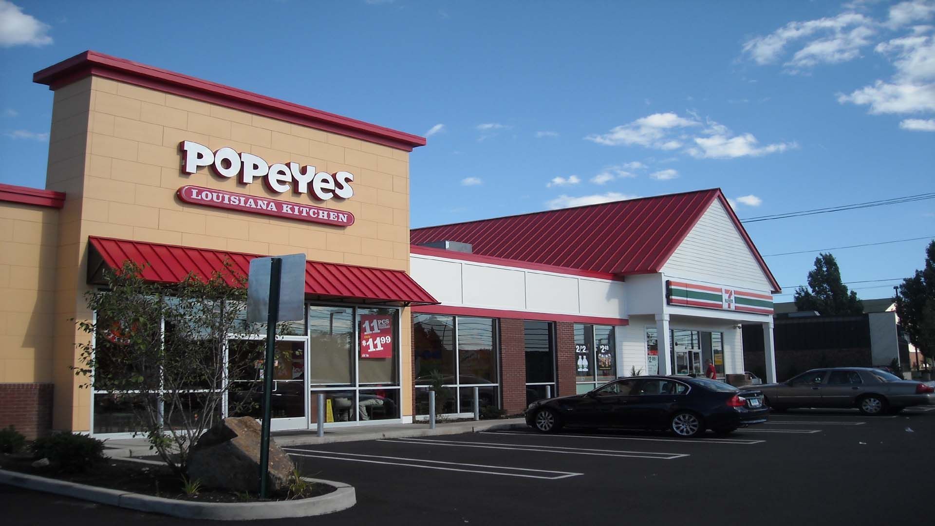 Popeyes restaurant and adjacent business, both with red roofs, in a parking lot on a sunny day.