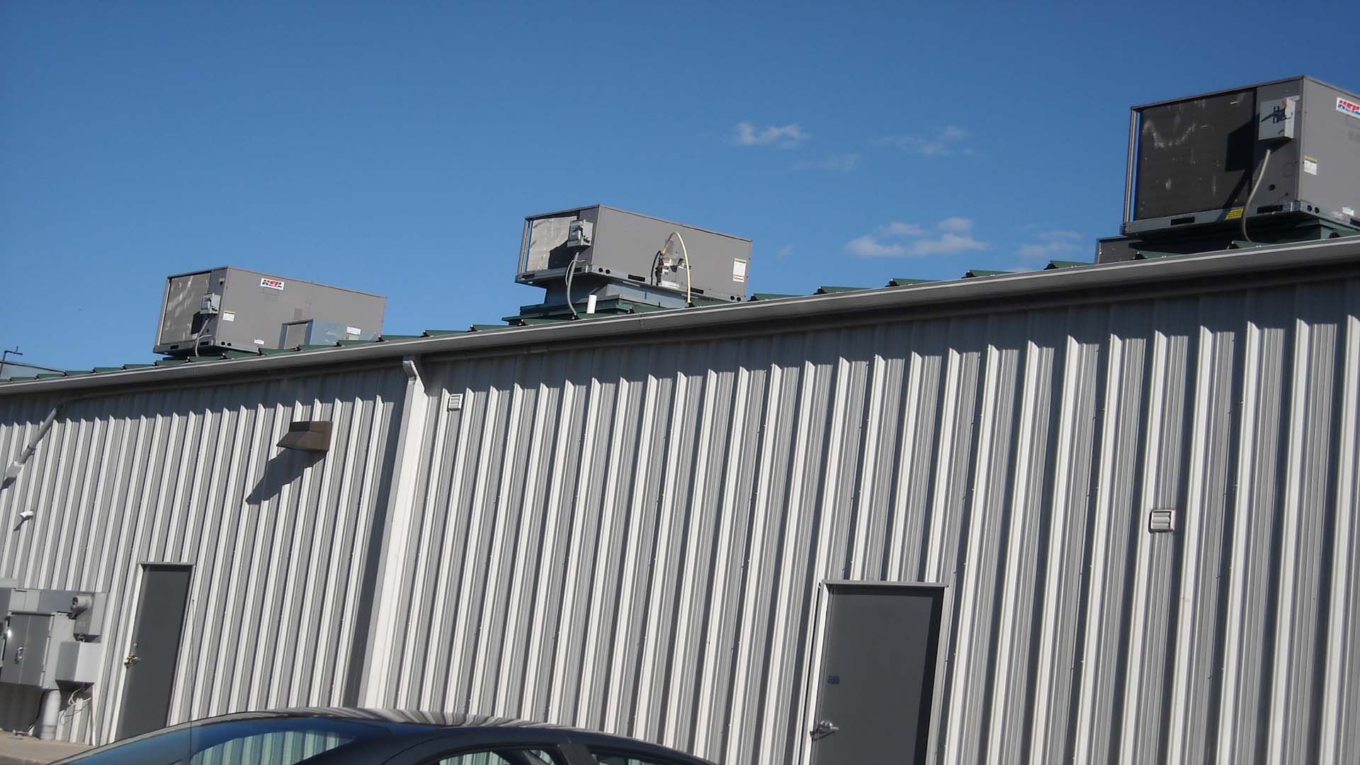 Building with metal siding and rooftop air conditioning units against a blue sky.