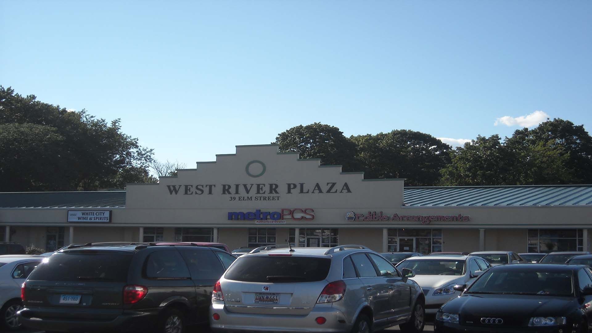 West River Plaza storefront, various businesses, parked cars, clear sky.