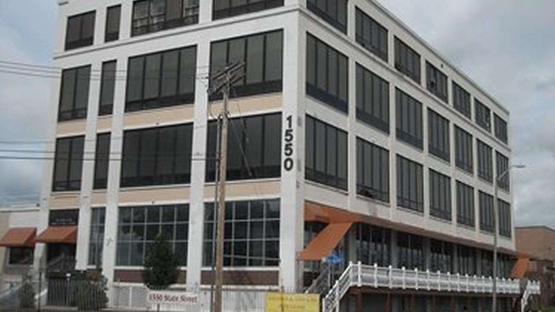 White building with large windows, 1550 on side. Orange awnings and stairs in front. Electric pole nearby.