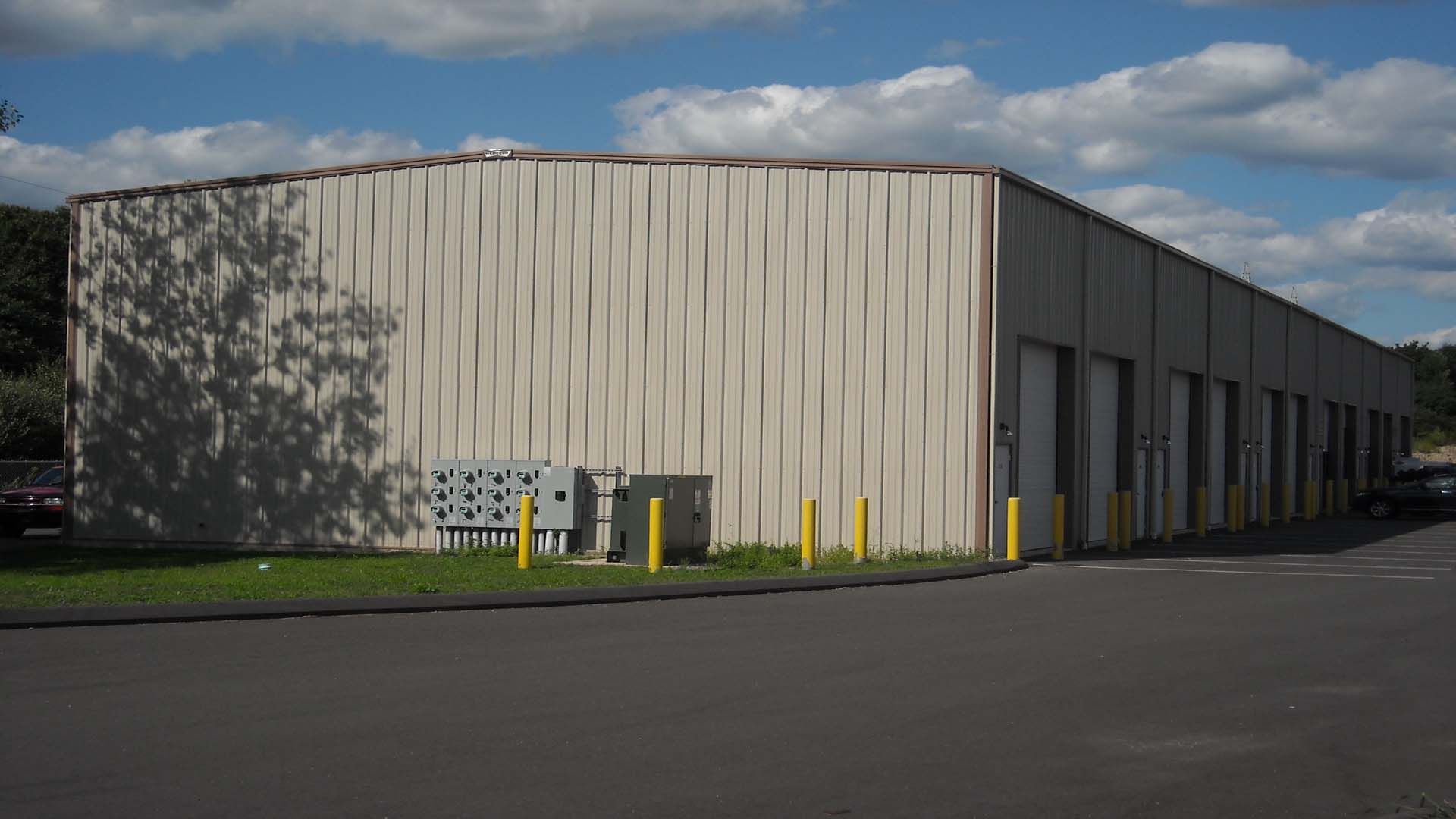 Warehouse with corrugated metal siding and multiple loading dock doors, on a paved lot under a blue sky.