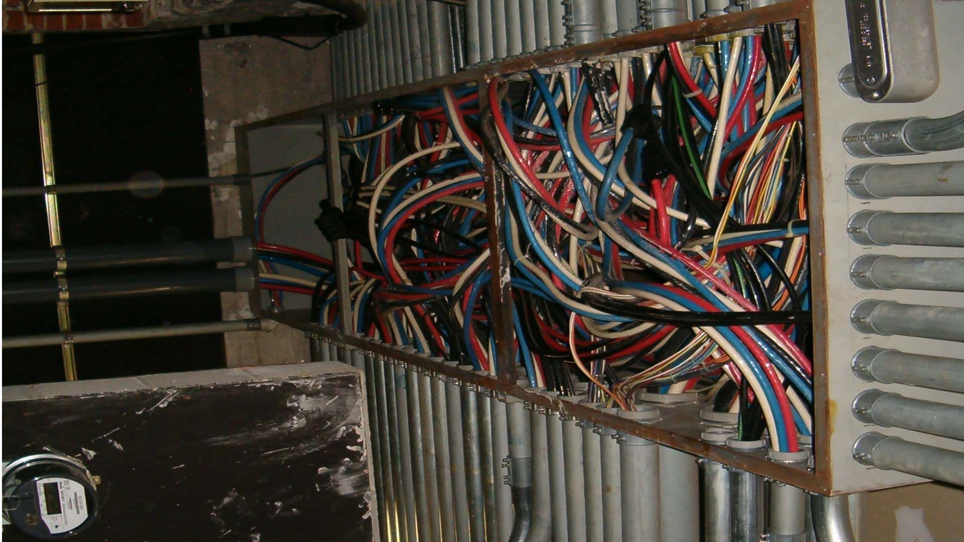Bundle of colorful electrical wires packed in a rectangular metal frame, inside a wall.