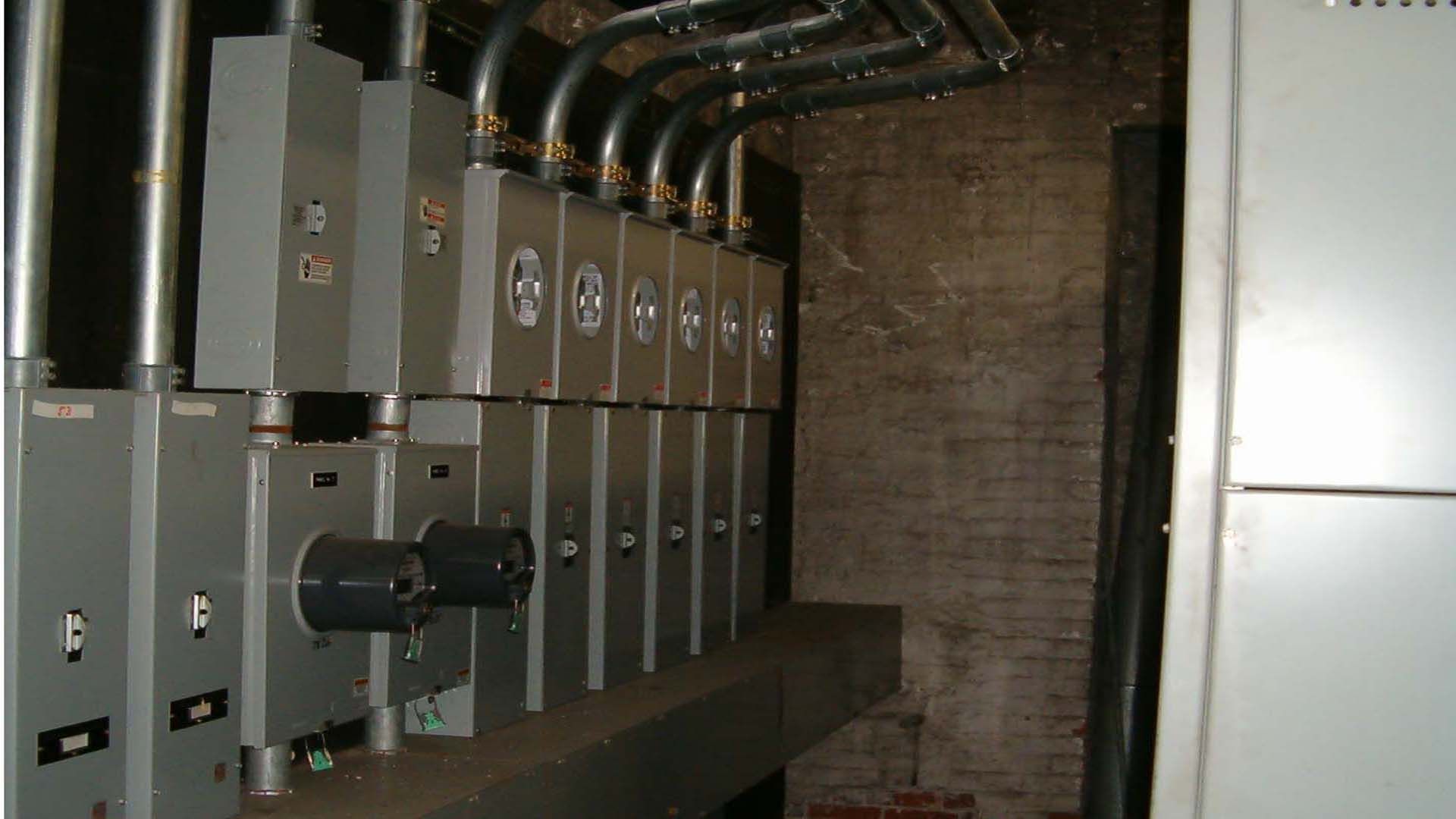 Electrical panel boxes with conduit and wiring against a brick wall.