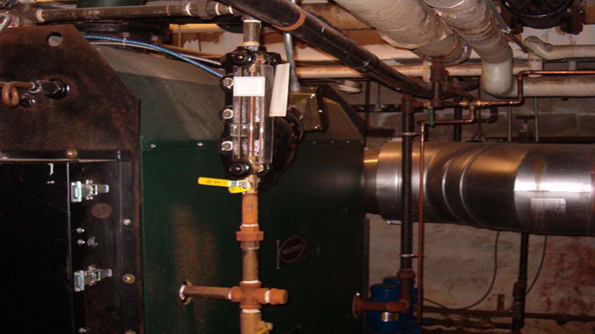 Green industrial boiler with pipes and a yellow valve in a utility room.