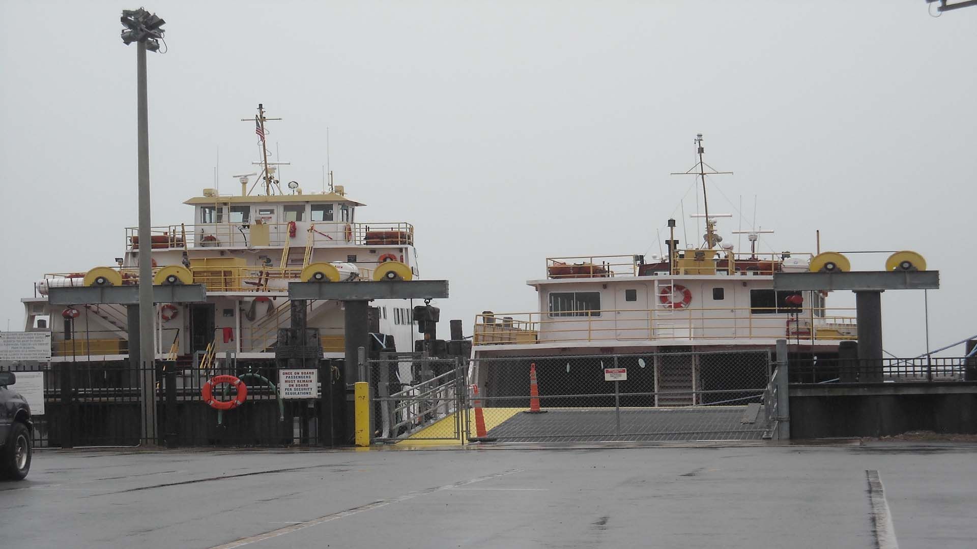 Two white and yellow ferry boats docked at a terminal on a gray, rainy day.