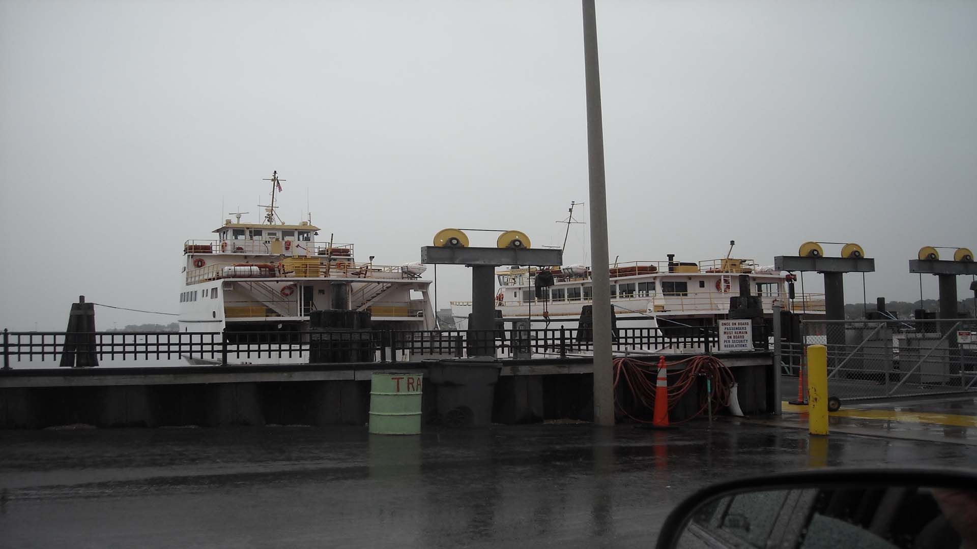 Ferry boats docked at a pier under a gray, overcast sky. Rainy conditions.