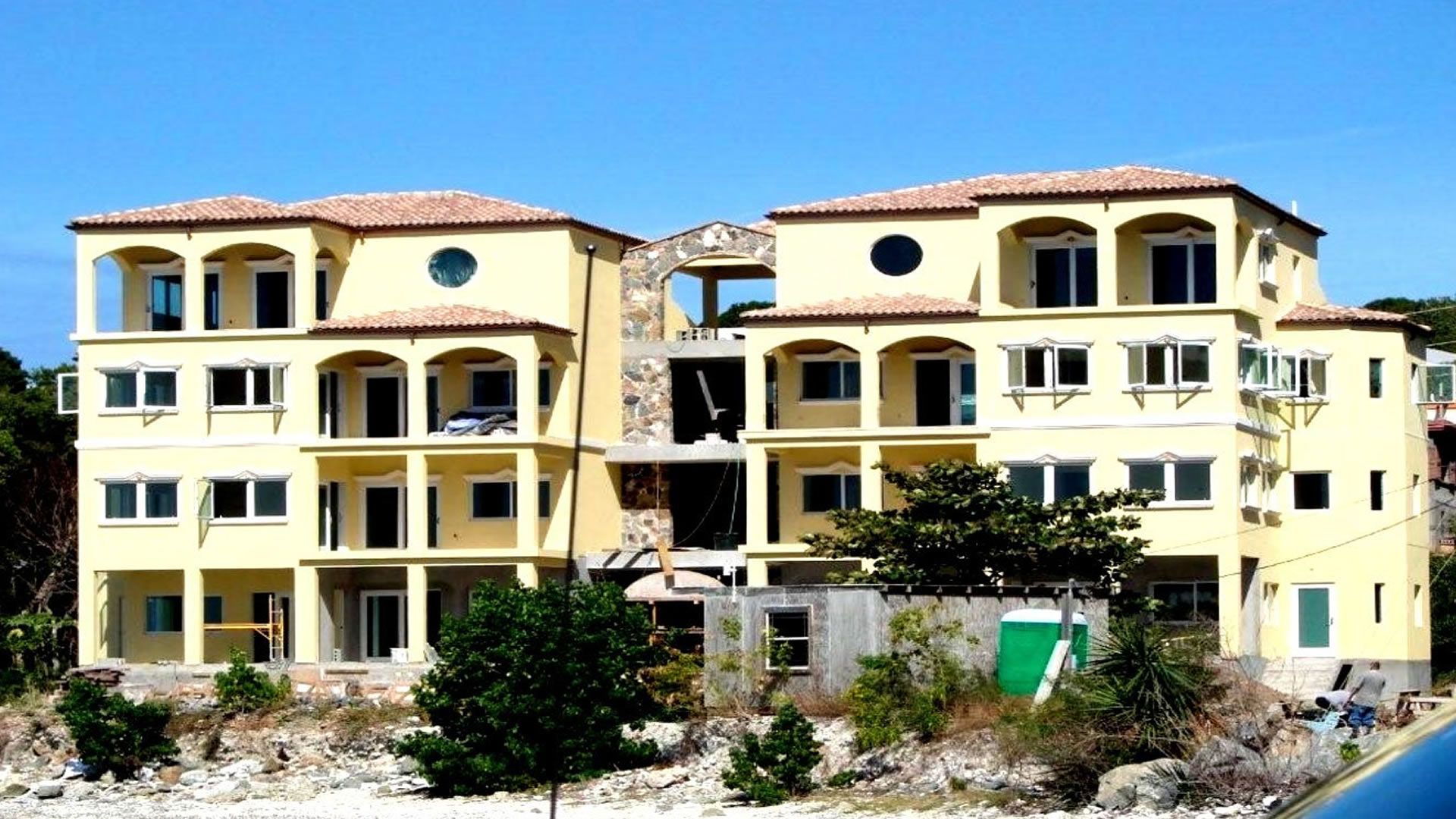 Yellow multi-story building under construction with arched doorways and windows, set against a clear blue sky.