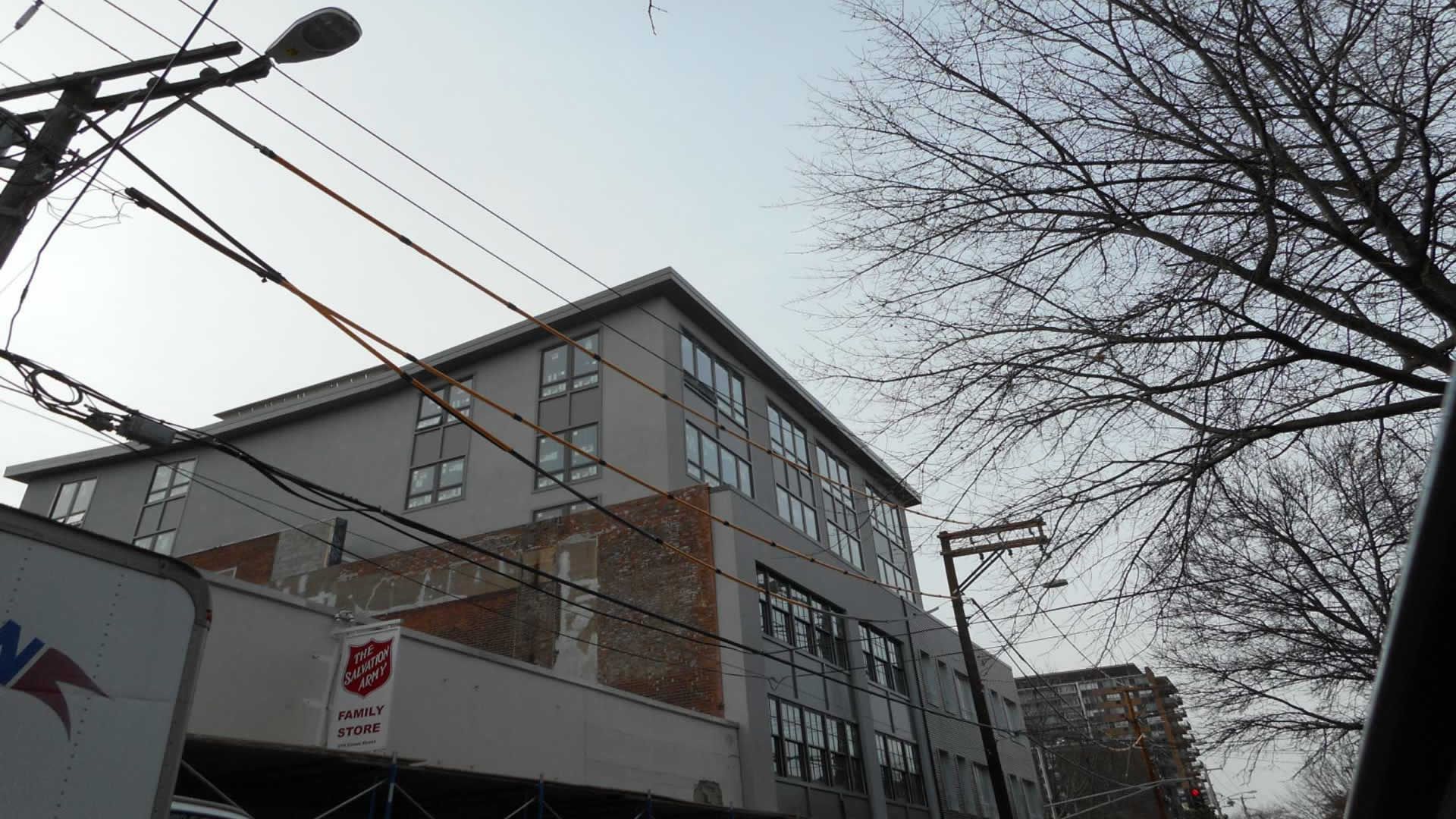 Modern apartment building, grey facade, with power lines and bare trees against a pale sky.