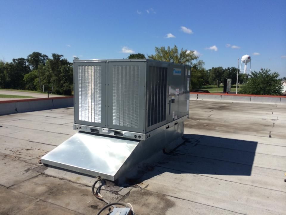 A large, grey commercial HVAC rooftop unit sits on a flat building roof under a clear blue sky.