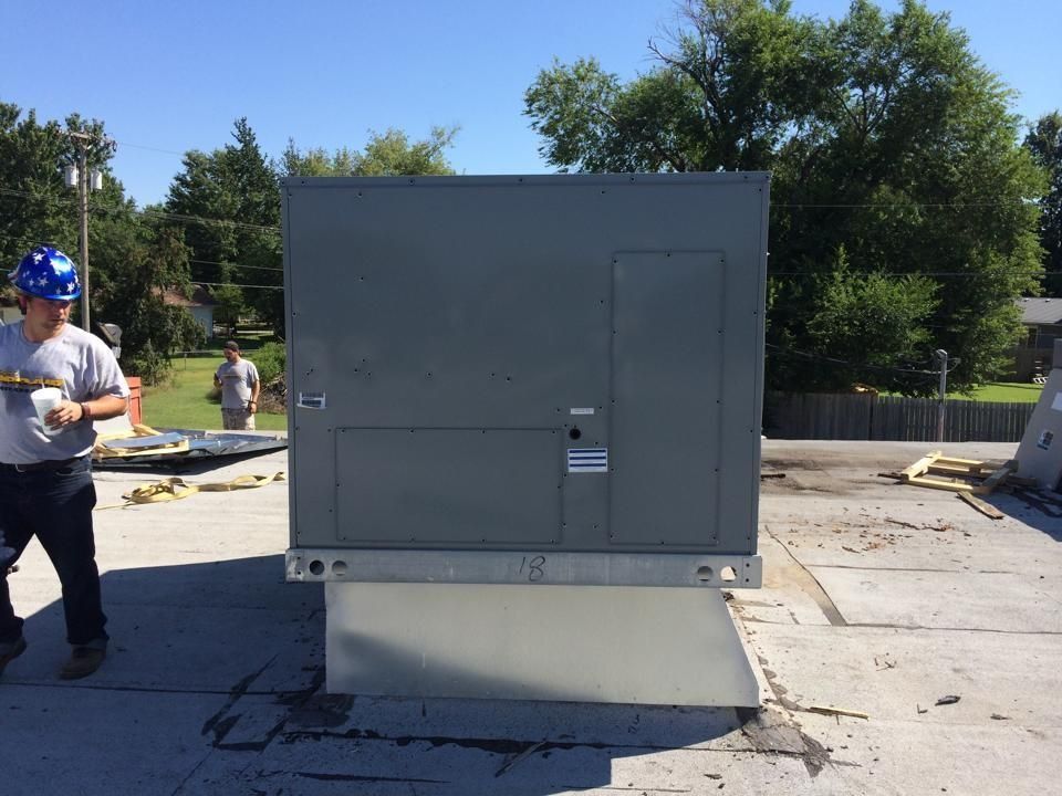Workers stand near a large commercial HVAC unit installed on a rooftop.