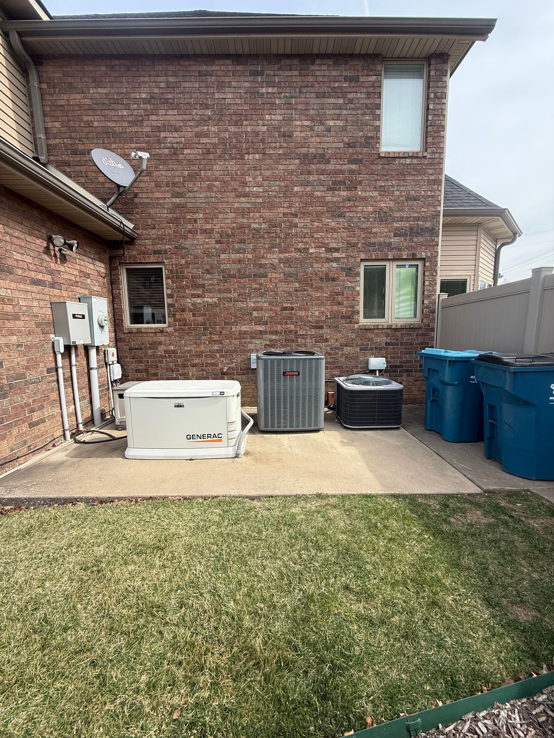 Brick house exterior featuring a generator, HVAC unit, utility boxes, and two blue trash bins on a concrete pad.