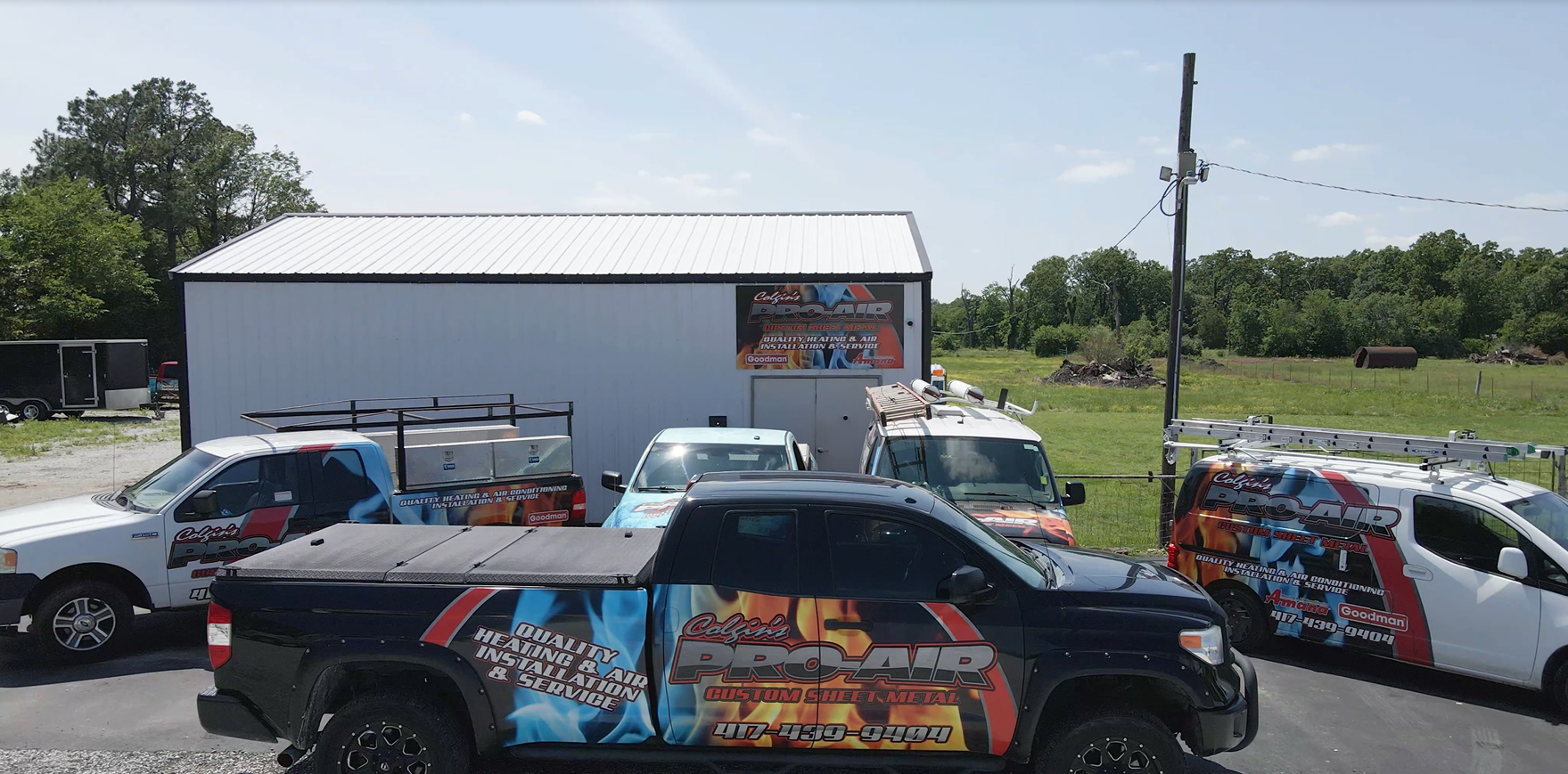 A fleet of branded work trucks parked in front of a white warehouse building on a sunny day.