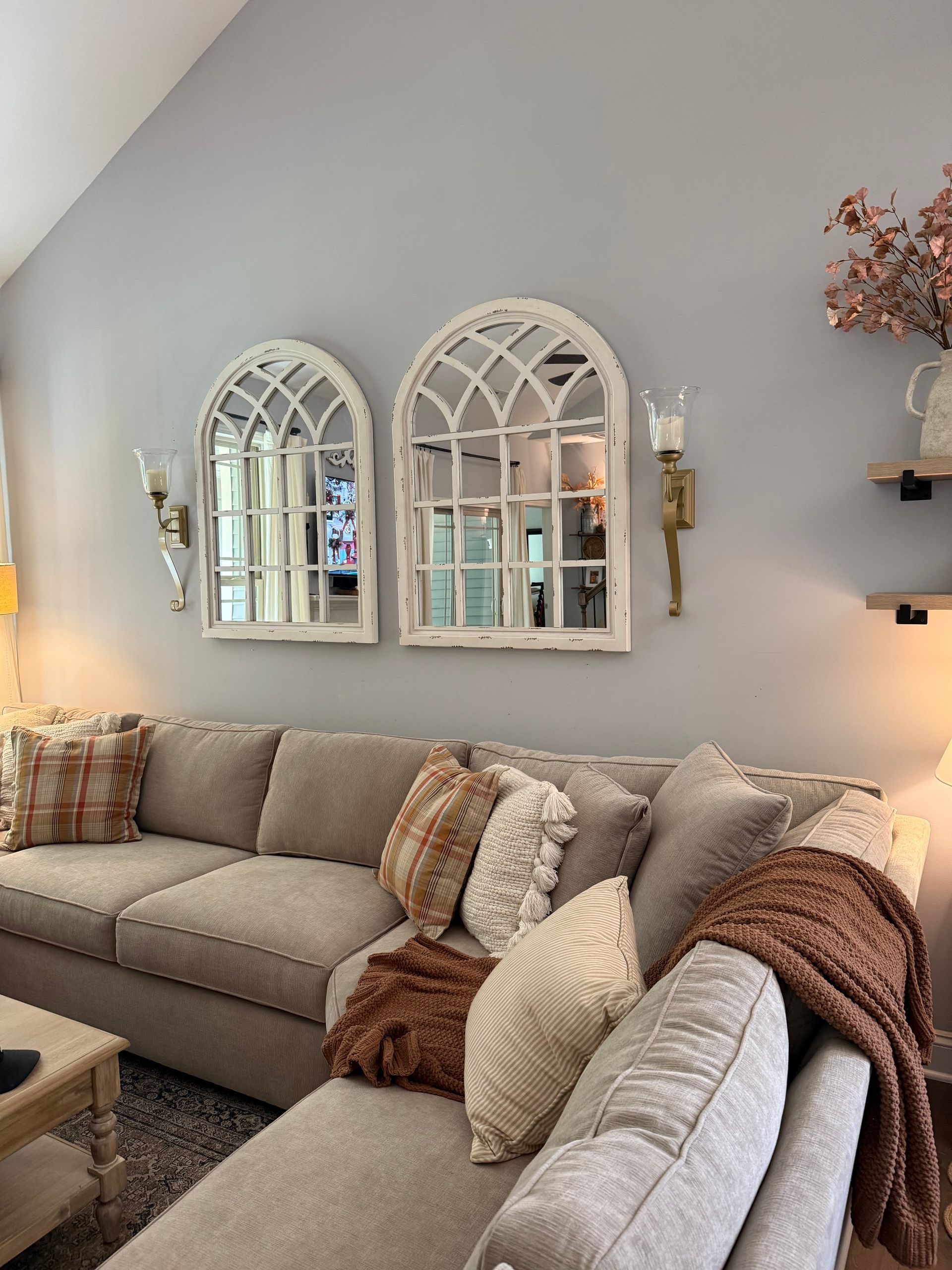 A living room with a sectional couch and two mirrors on the wall.