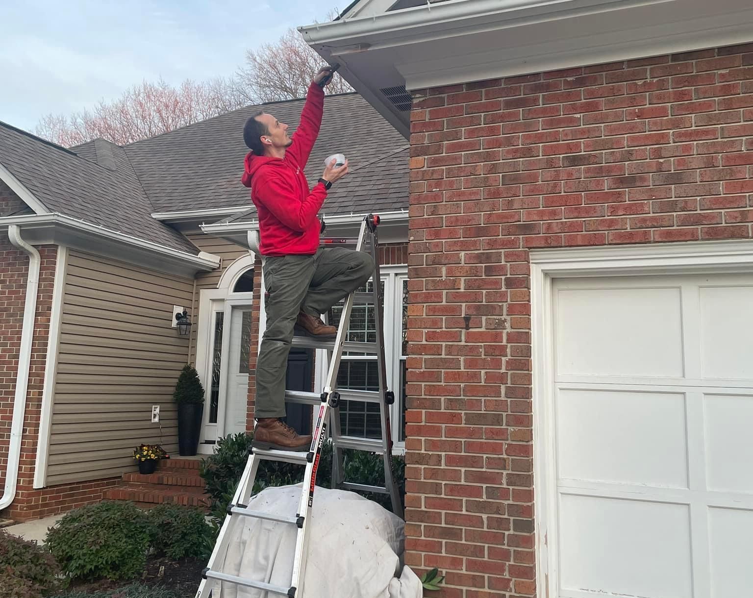 A man is standing on a ladder in front of a brick house.