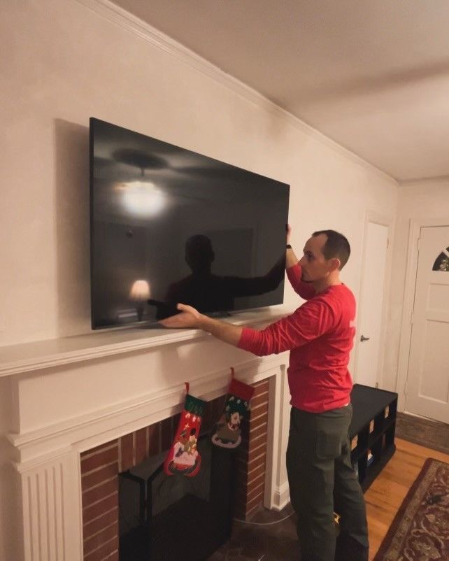 A man in a red shirt is installing a flat screen tv