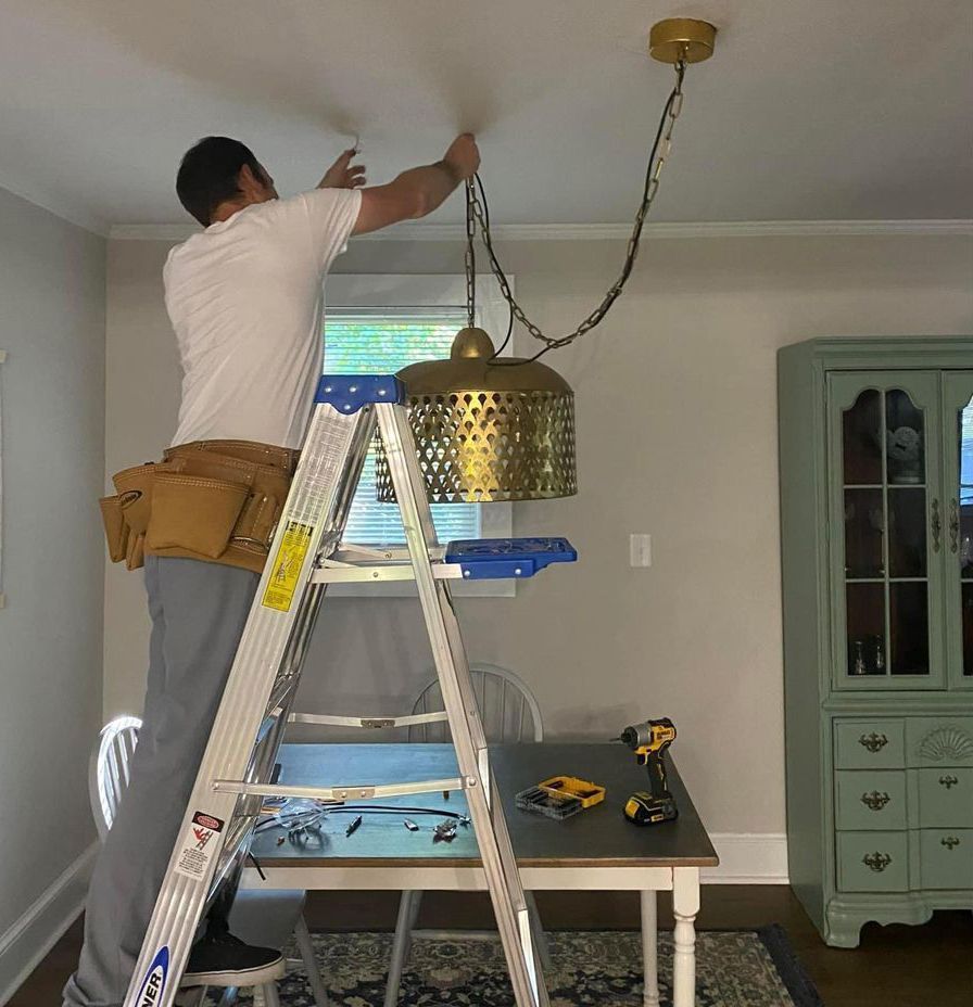 A man is standing on a ladder fixing a light fixture