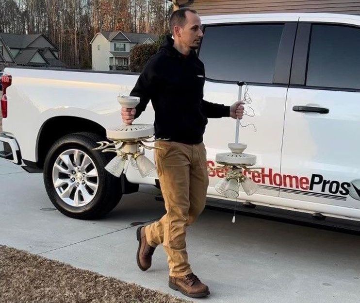 A man is carrying a ceiling fan in front of a truck.