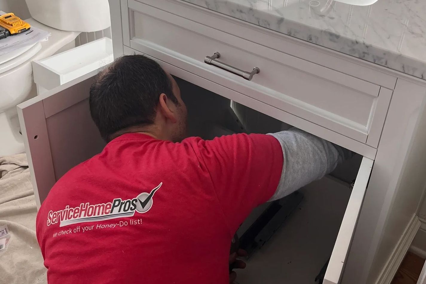 A man in a red shirt is fixing a sink in a bathroom.