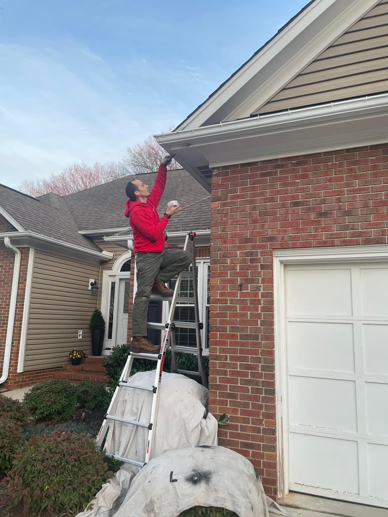 A man is standing on a ladder on the side of a brick house.