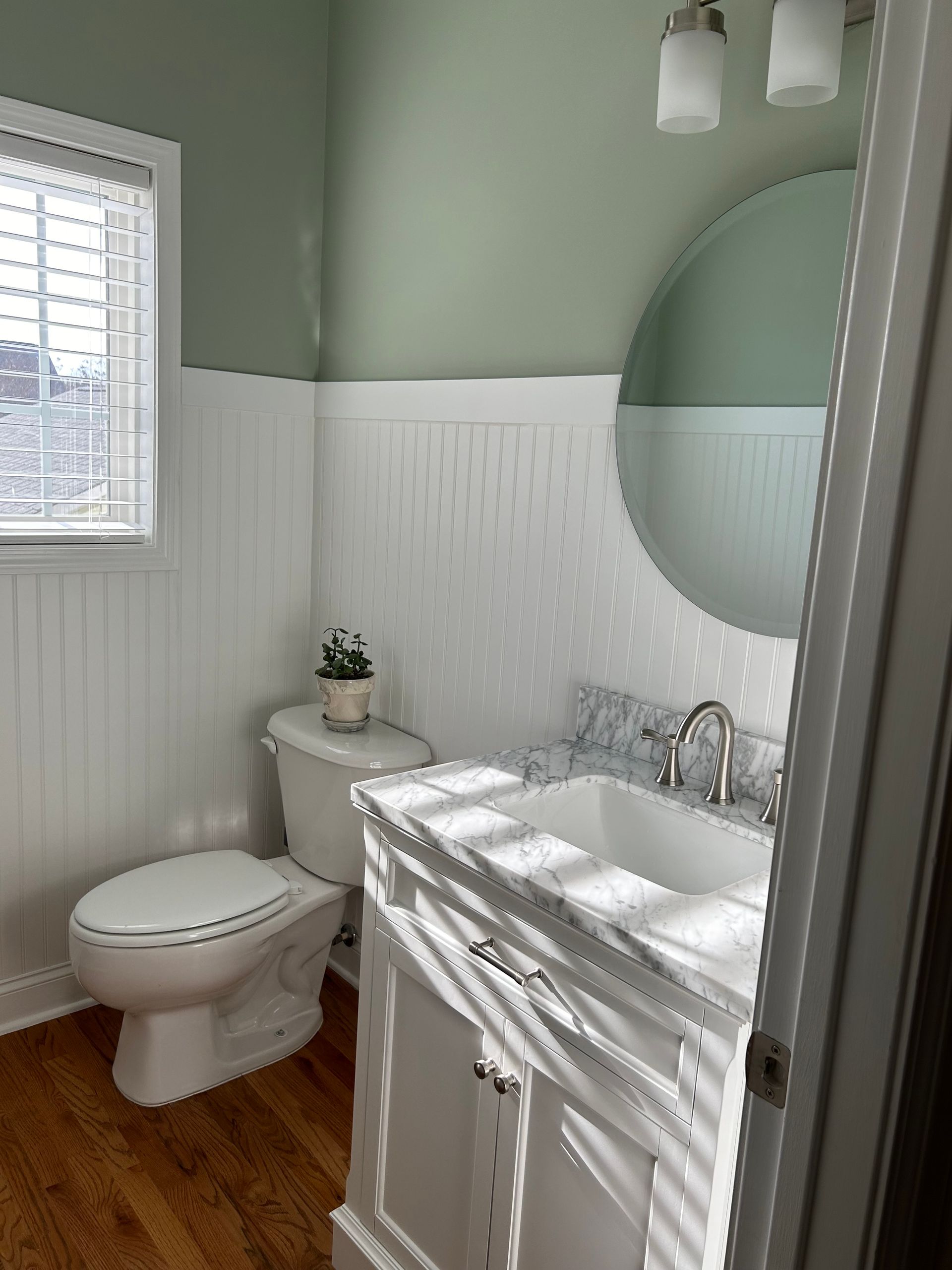 A bathroom with a toilet , sink , mirror and window.