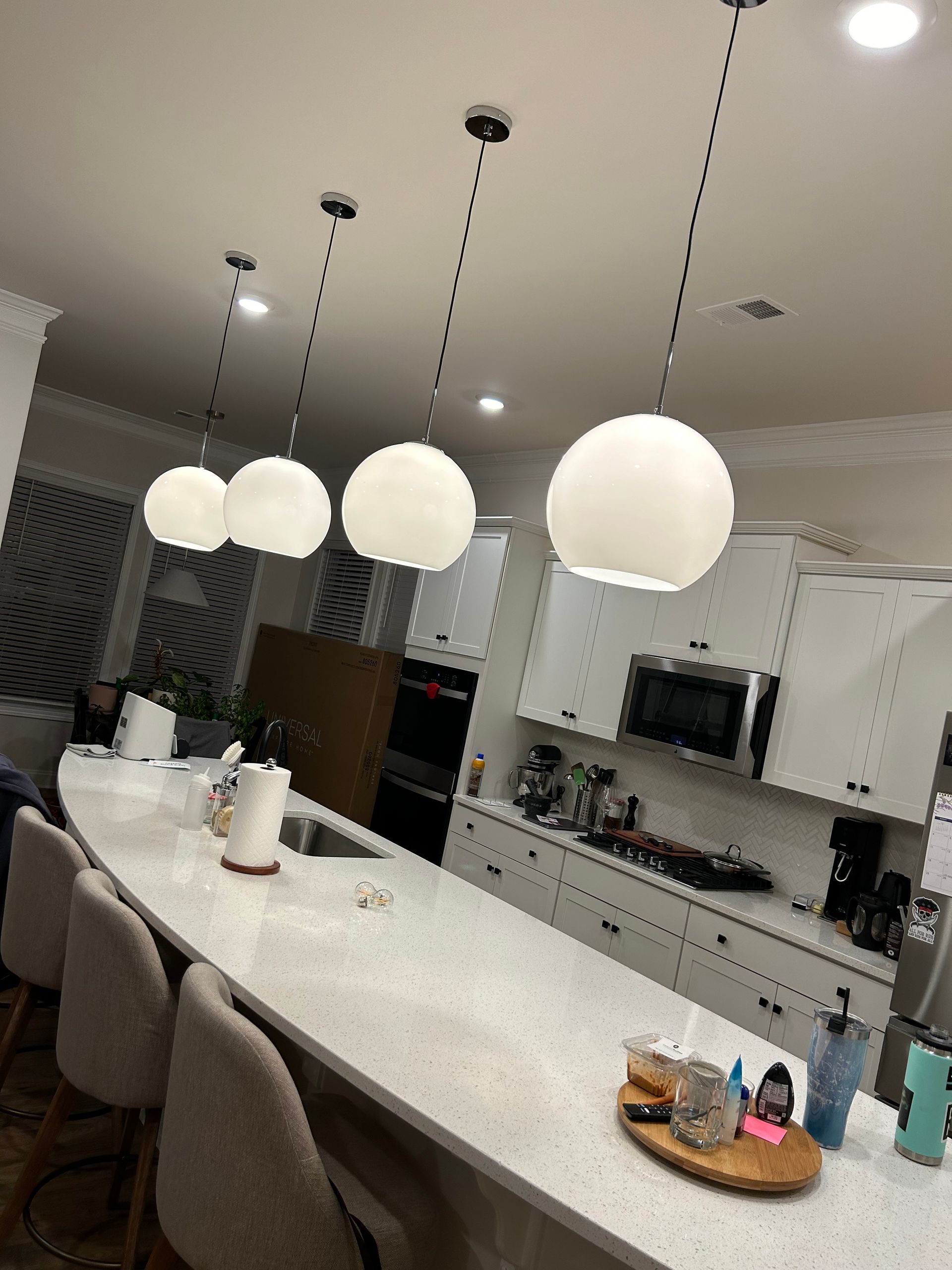 A kitchen with white cabinets , white counter tops , and white pendant lights hanging from the ceiling.