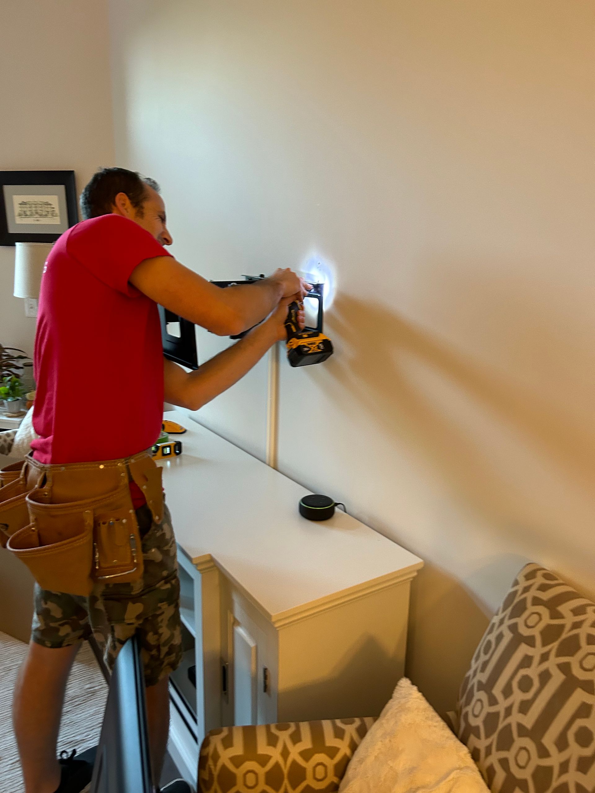 A man in a red shirt is working on a wall with a drill