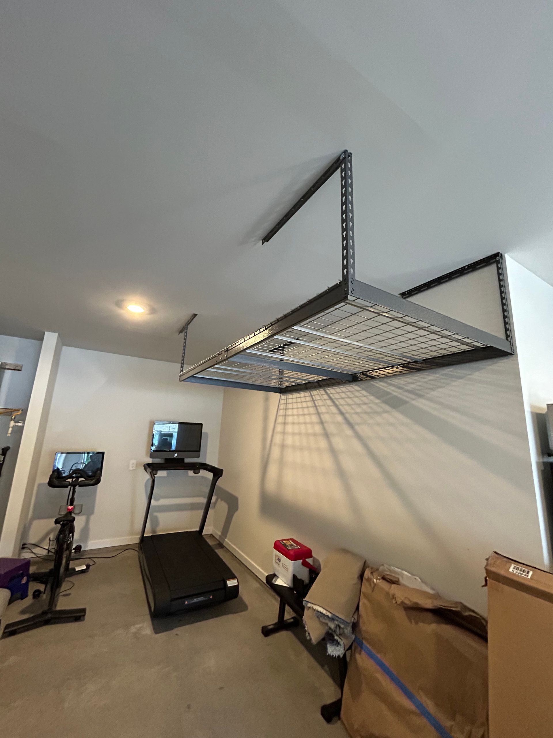 A treadmill is hanging from the ceiling of a garage.