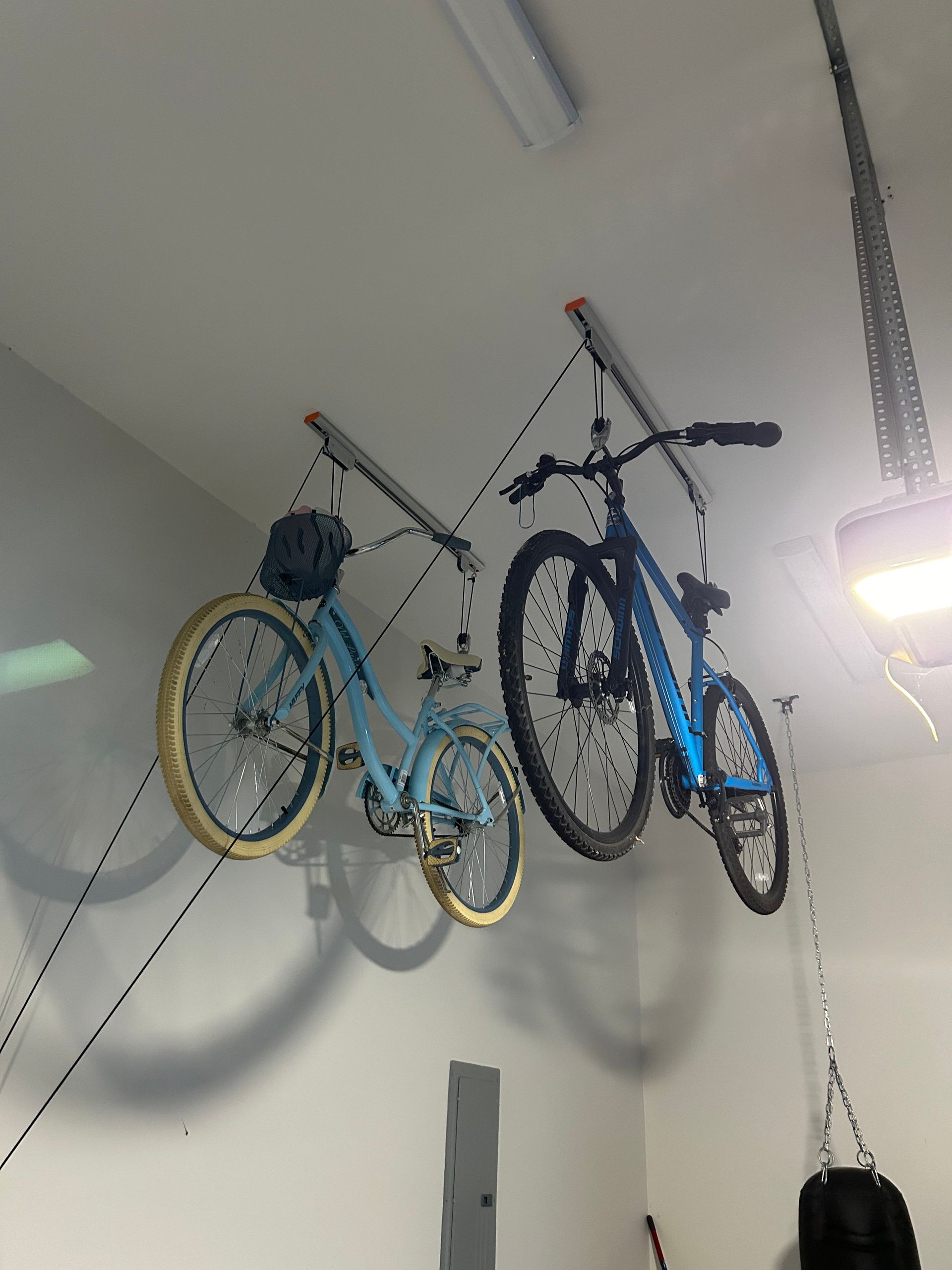 Two bicycles are hanging from the ceiling in a garage