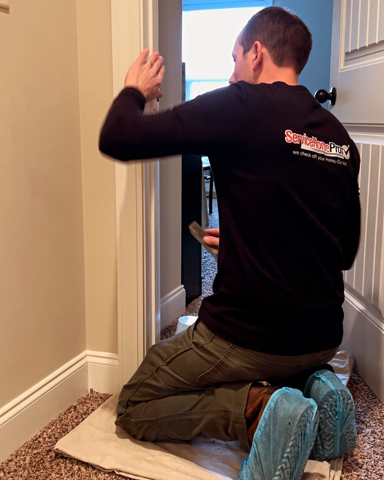 A man is kneeling down in front of a door holding a hammer.