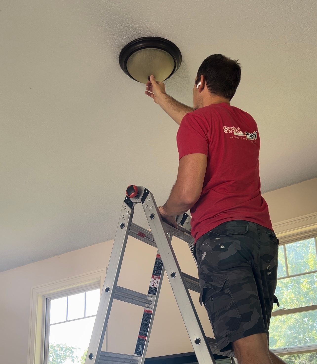 A man is standing on a ladder fixing a light fixture on the ceiling.