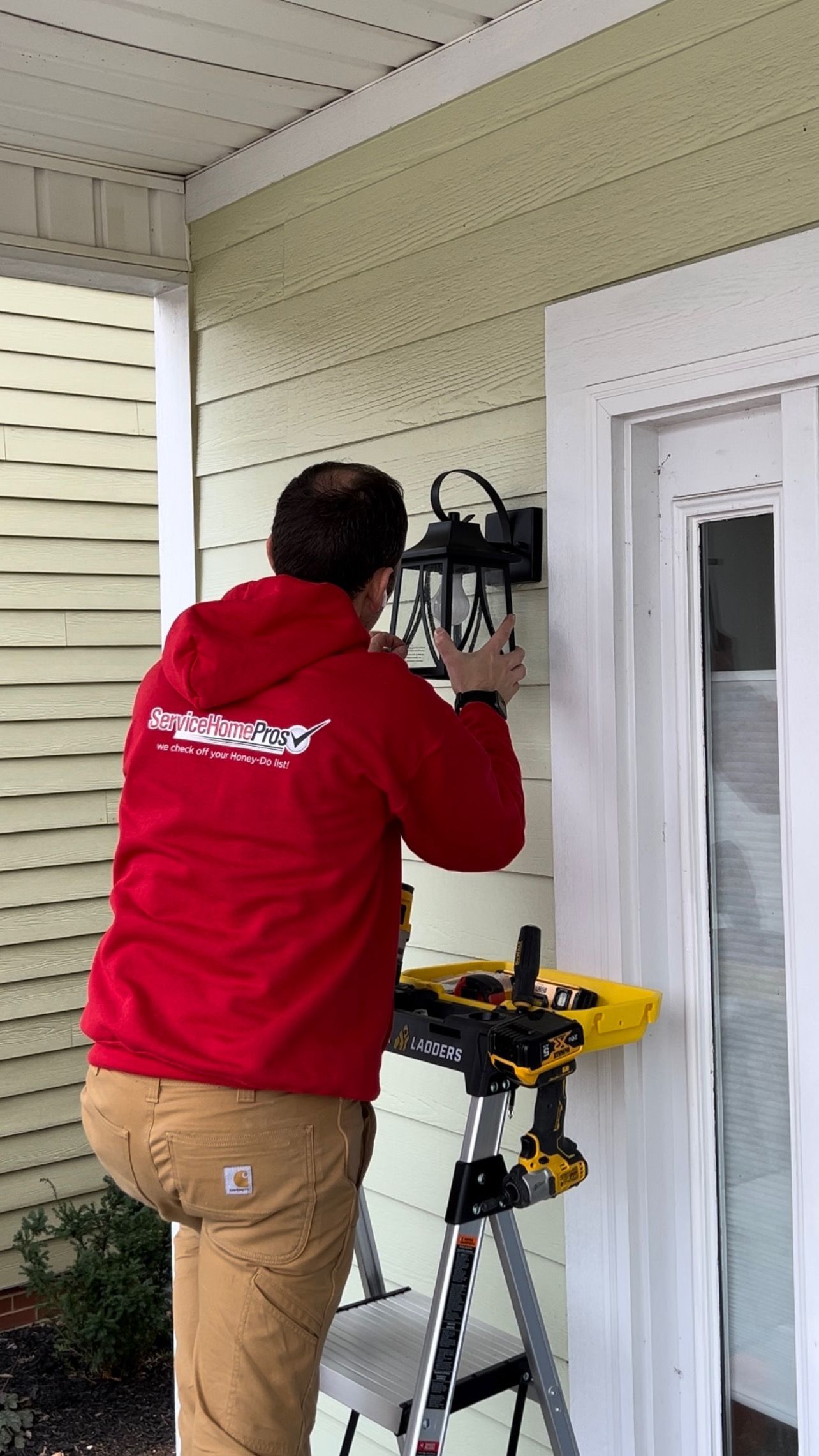 A man is standing on a ladder fixing a light on the side of a house.
