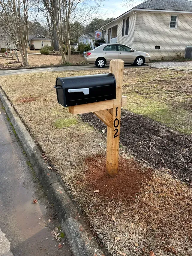 A black mailbox is sitting on a wooden post in front of a house.